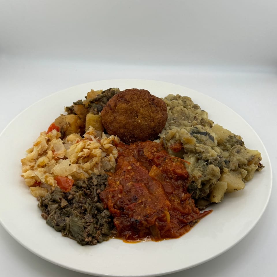 A white plate holds a variety of cooked dishes, including a fried patty, stewed vegetables, and sauces.