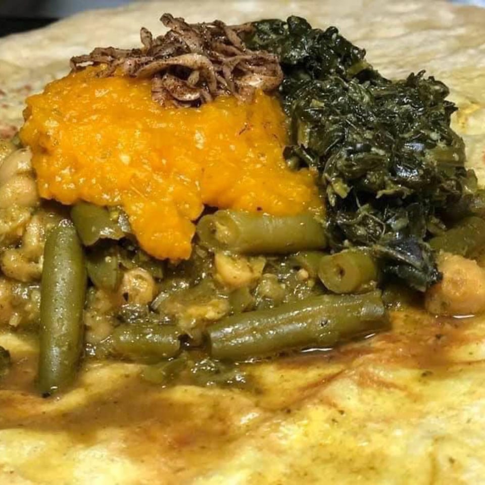 A close-up of a colorful dish with green beans, dark leafy greens, and orange puree.