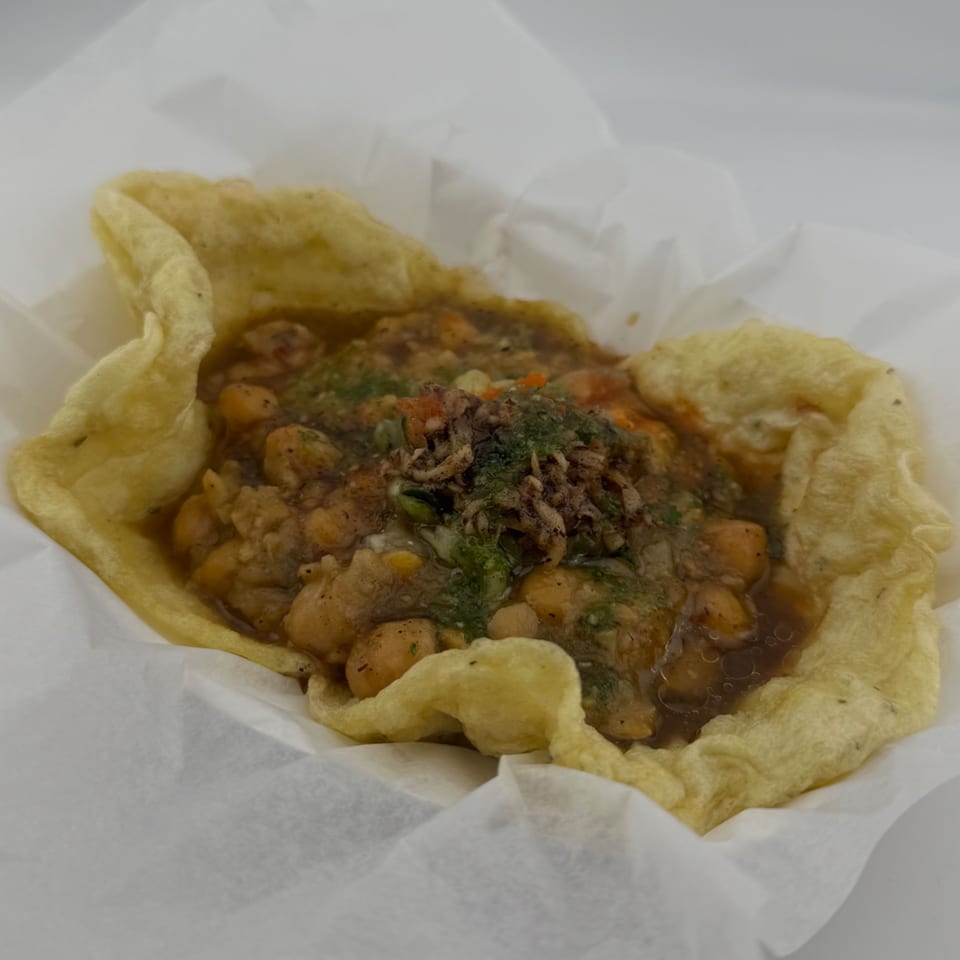 A close-up of a fried flatbread bowl filled with chickpeas in a savory sauce, garnished with herbs.