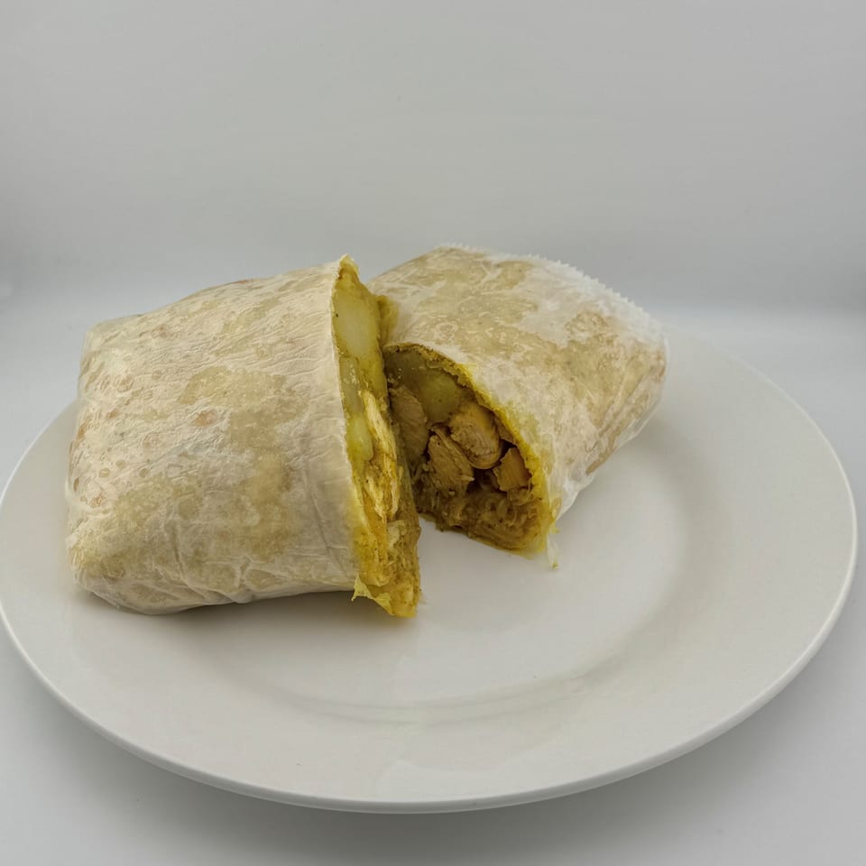 A chicken and potato roti, cut in half, revealing the yellow curry filling on a white plate.