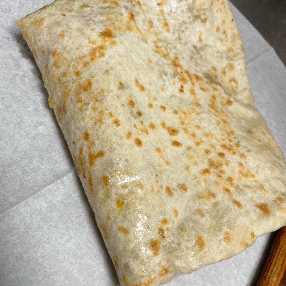 A close-up of a golden-brown quesadilla or burrito, folded and resting on white parchment paper.